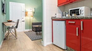 Une cuisine de taille réduite avec des meubles de couleur rouge, un réfrigérateur blanc et un four à micro-ondes posé sur le plan de travail.