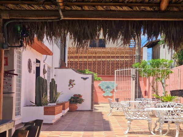 Un patio al aire libre con techo de paja, paredes blancas y un portón decorativo.