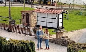 A small stone building with a red-tiled roof, a wooden fence, and a sign that reads 'Visitors Welcome.'