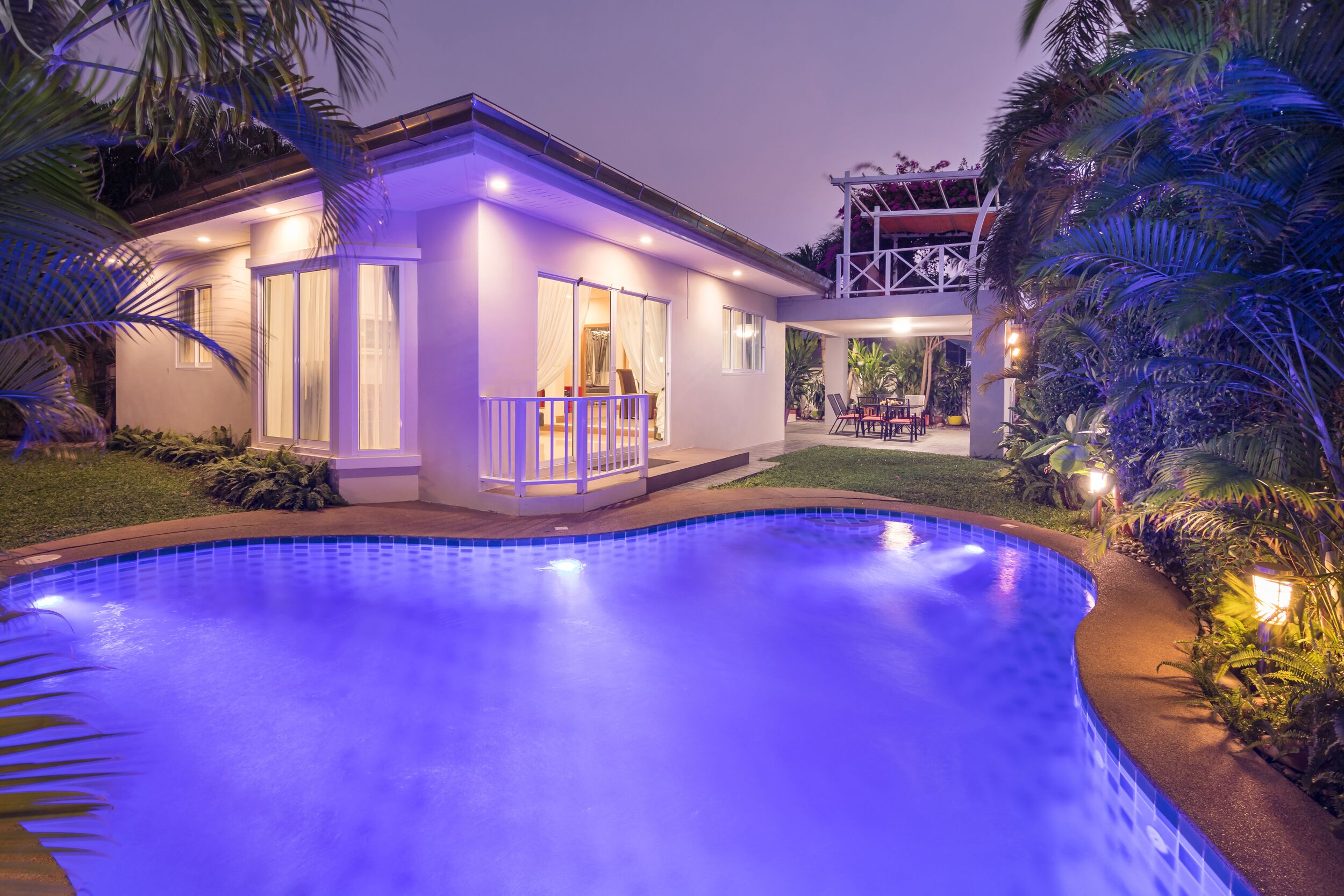 A modern house with a swimming pool, surrounded by tropical plants.