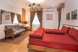A hotel room with a bed, a sofa, a small table, a lamp, a mirror, and artwork on the walls.