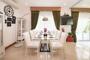 A dining area with a glass table, white chairs, and a modern chandelier.