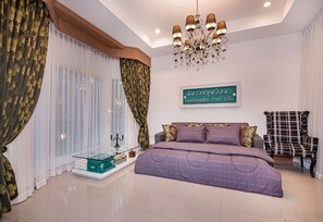 A bedroom with a glass coffee table, a bed with a purple bedspread, a chandelier, and a sign on the wall.