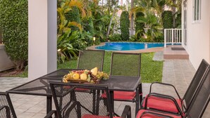 Una terrazza esterna con un tavolo apparecchiato per mangiare, circondata da sedie con cuscini rossi, e una piscina sullo sfondo.