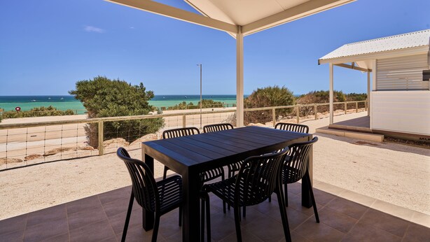 A covered outdoor patio with a table and chairs, overlooking a beach and ocean.