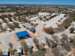 Vista aérea de un camping con vehículos recreativos, una tienda azul grande y un edificio con techo inclinado.