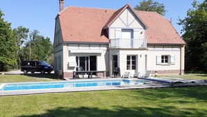 Ein zweistöckiges Haus mit rotem Ziegeldach, einer Veranda und einem Swimmingpool.