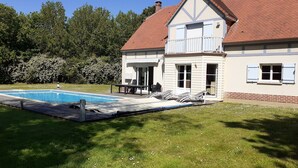 Ein zweistöckiges Haus mit Swimmingpool, überdachter Terrasse und Garten.