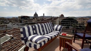 A rooftop terrace with a striped sofa and chairs, overlooking a cityscape with historic buildings. - Penthouse Hilife Panoramic Terrace (Florence)