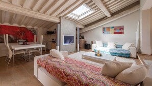 A cozy loft bedroom with a sloped ceiling, a skylight, a bed with patterned bedding, a white sofa, and a dining area with a table and chairs. - Penthouse Hilife Panoramic Terrace (Florence)