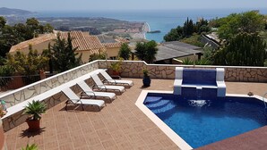 Une piscine sur le toit, dotée de chaises longues, d’un petit élément décoratif aquatique et offrant une vue sur l’océan et le paysage environnant.