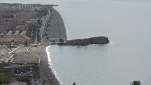 Un paysage urbain côtier avec une plage, des bâtiments et un promontoire rocheux.