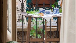 A balcony with a table set for tea, surrounded by potted plants and a view of a building.