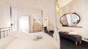 A bedroom with a canopy bed, a bedside table with a tray of tea and pastries, a dresser, and a mirror on the wall.