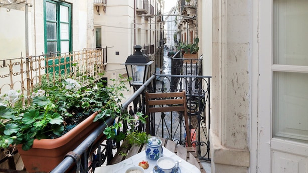 A narrow urban street with buildings on either side, a small table with a white tablecloth, and potted plants.