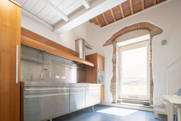 Une cuisine moderne dotée d’appareils électroménagers en acier inoxydable, d’un plan de travail en bois et d’une arche en pierre donnant accès à un balcon.