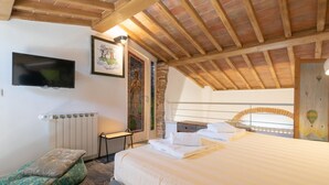 Un dormitorio con cama, televisor, radiador, una mesita y ventana con vistas.