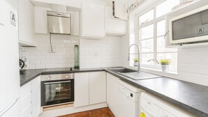 Eine moderne Küche mit weißen Schränken, einem Edelstahlbackofen, einem Geschirrspüler und einem Fenster mit Blick.