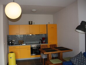 A compact kitchen with yellow cabinets, a tiled backsplash, a stove, and a dining area with a table and chairs.