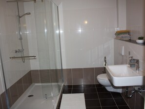 Ein modernes Badezimmer mit Duschkabine aus Glas, einem weißen Waschbecken und einer Toilette.