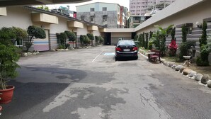 A parking area with a car, potted plants, and a building with a ramp. - Treasure Island Hotel - Xinfu (Kaohsiung)