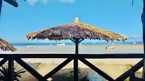 Vista de playa con una sombrilla de paja, barcos en el agua y una orilla arenosa.