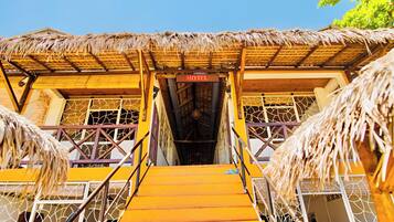 A hotel entrance with a thatched roof, wooden stairs, and a sign indicating the hotel's name.