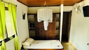 A hotel room with a bed, two pillows, a hanging light fixture, a wooden wardrobe, and a fan. - Tropical Paradise Nosy Be (Nosy Be)