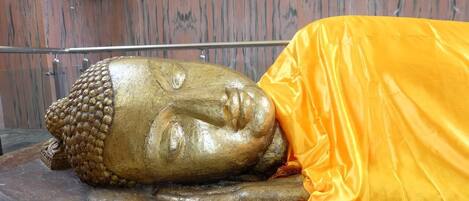A golden Buddha statue with a yellow cloth draped over it, set against a wooden wall background.