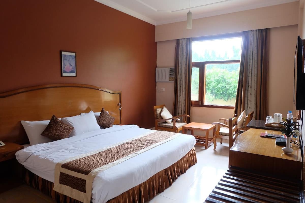 Una habitación de hotel con una cama grande, un cabecero de madera, un escritorio con una silla, un televisor y una ventana con cortinas.