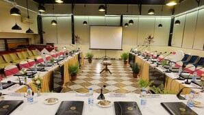 Un salón de conferencias con suelo a cuadros, varias filas de sillas, tarjetas de identificación, botellas de agua y portátiles.