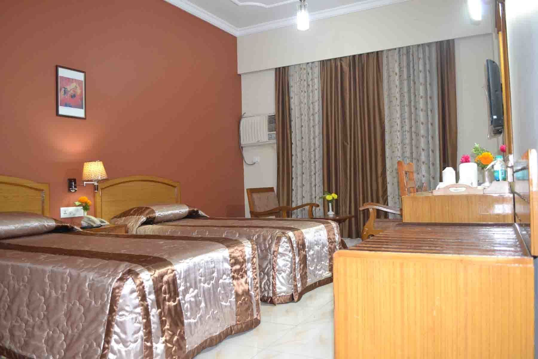 A hotel room with two beds, a desk, a chair, a mirror, and a window with curtains.