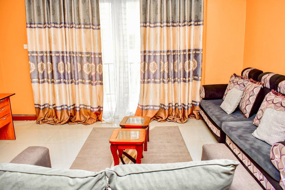A living room with a sofa, two small tables, and a large window with curtains.