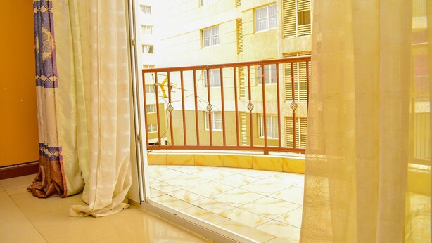 Un balcon doté d’une rambarde en métal, d’un sol carrelé et offrant une vue sur un immeuble à multiples fenêtres.