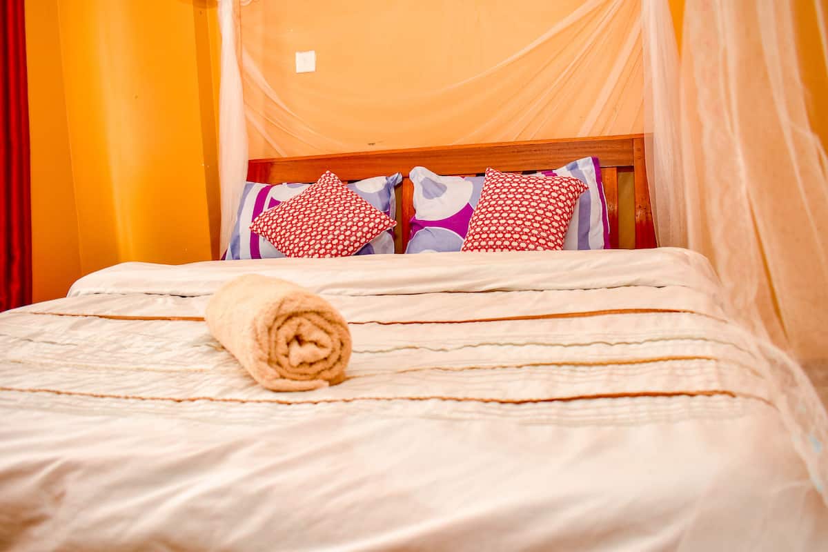 A neatly made bed with a rolled towel, a wooden headboard, and a canopy.