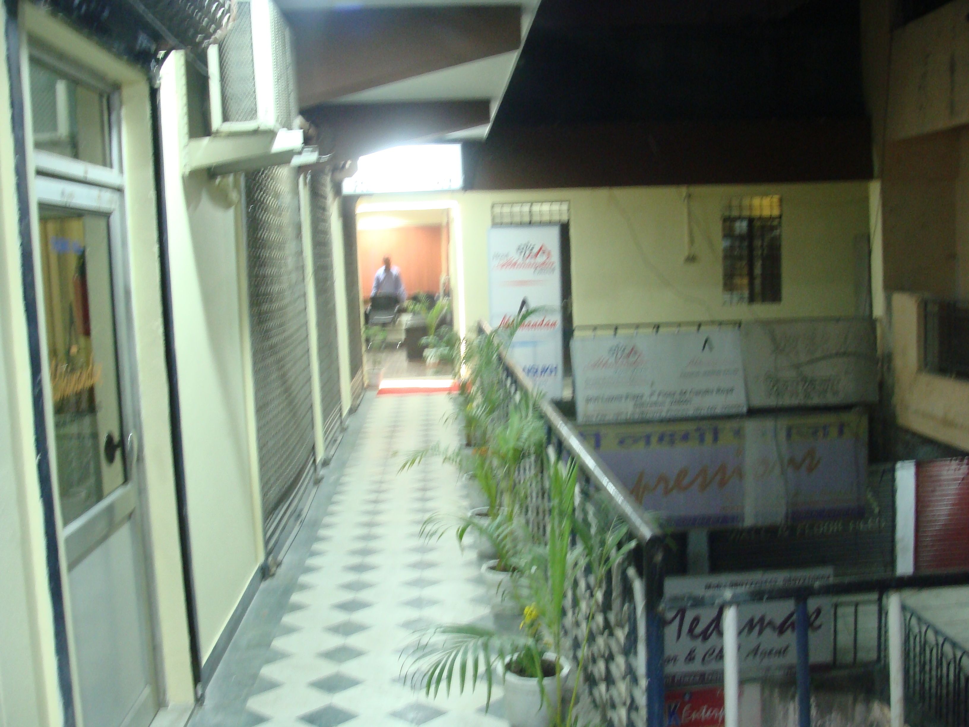 A corridor with a checkered floor, potted plants, and boxes stacked against the wall.
