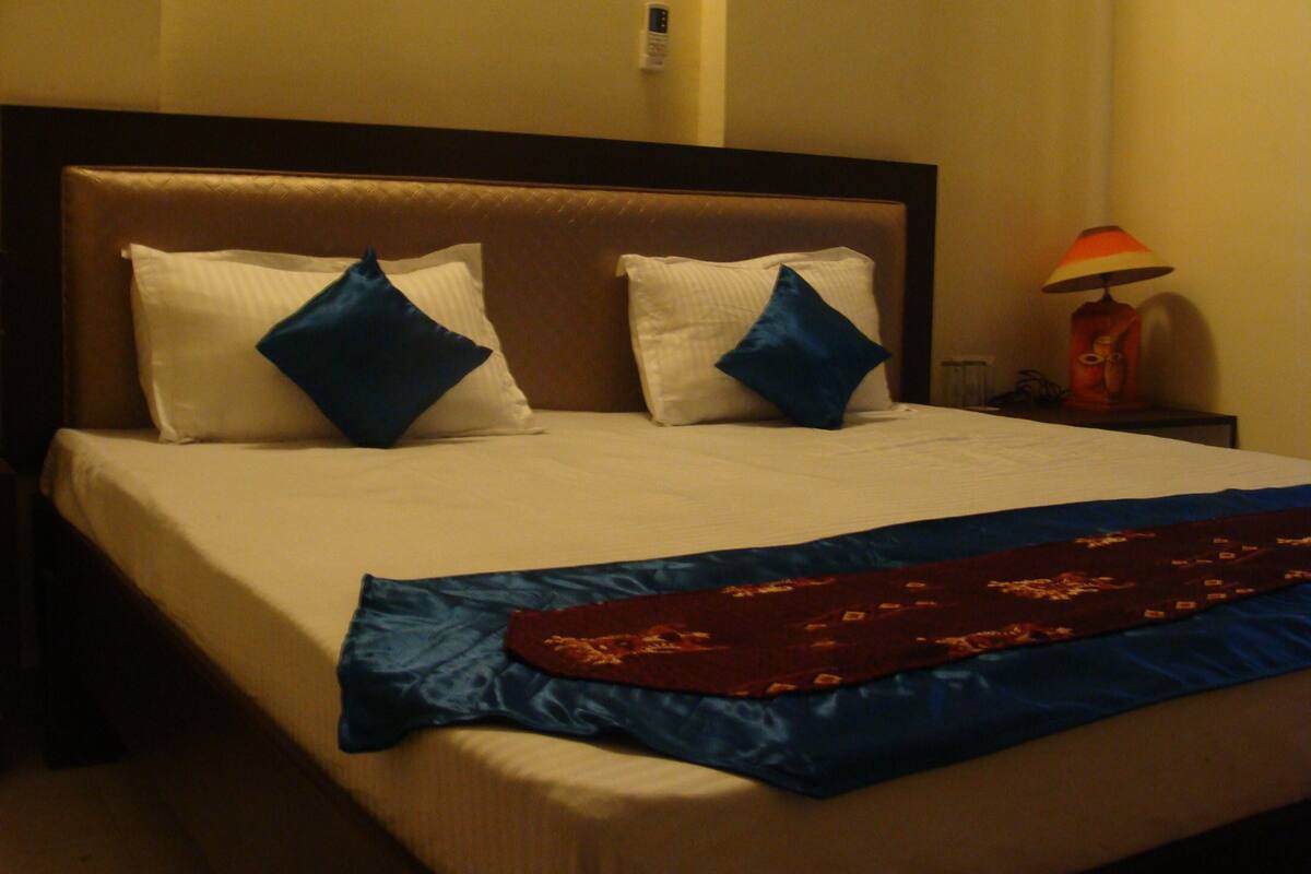 Une chambre d’hôtel avec un grand lit, deux oreillers, une lampe et une couverture.