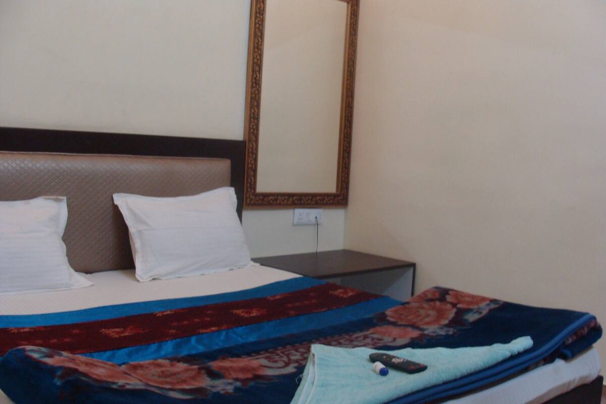 Une chambre d’hôtel avec un lit, des oreillers, une couverture, une télécommande et un miroir au mur.