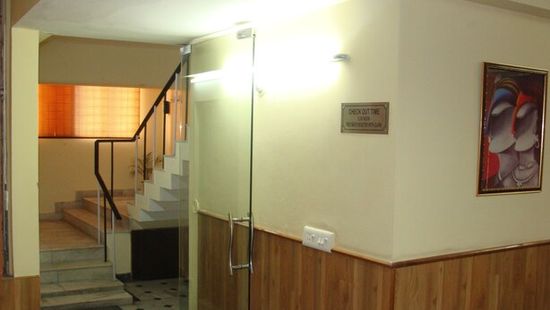 Un hall d’hôtel avec un escalier, un panneau indiquant l’heure limite pour quitter la chambre, et un tableau encadré accroché au mur.