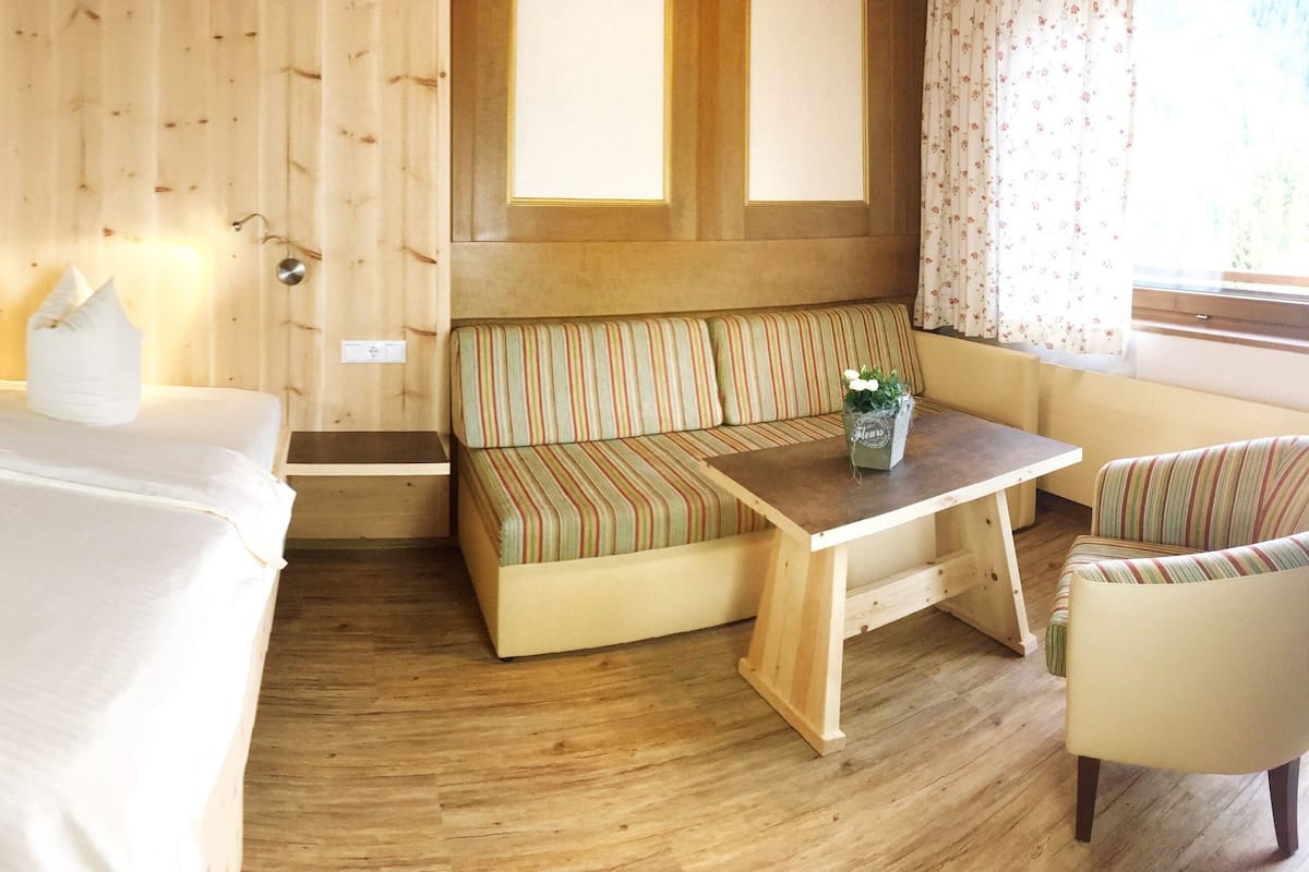 A wooden-paneled room with a bed, a bench, a table, and a chair.