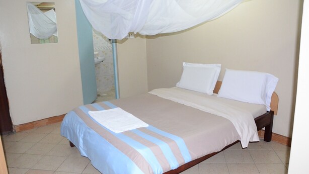 A bed with a white canopy, a blue and beige striped bedspread, and a white pillow. - Starehe link hotel (Nairobi)