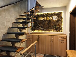 A modern staircase with black cushioned steps and wooden railings, leading to a room with a moss wall and a sign that reads "PENSION". - Pension 19 (Pirna)