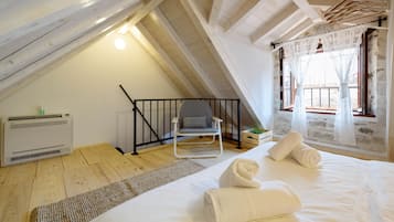 Un dormitorio ático acogedor con suelo de madera, una cama blanca, una silla y un ventanal con cortinas translúcidas.