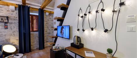 A cozy room with a wooden ceiling, stone walls, a TV, a desk with a plant, and a coffee table.