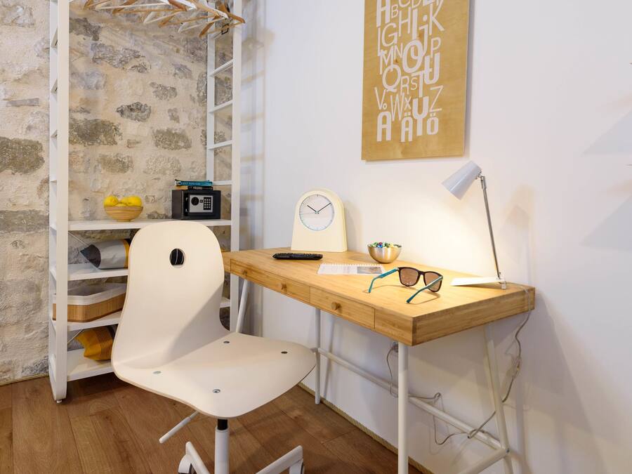 A modern office space with a white desk, a white office chair, a wooden ceiling, a stone wall, and a wall-mounted shelf with a radio and decorative items.