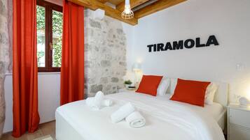 A bedroom with a bed, red curtains, a stone wall, and a sign that reads "TIRAMOLA".