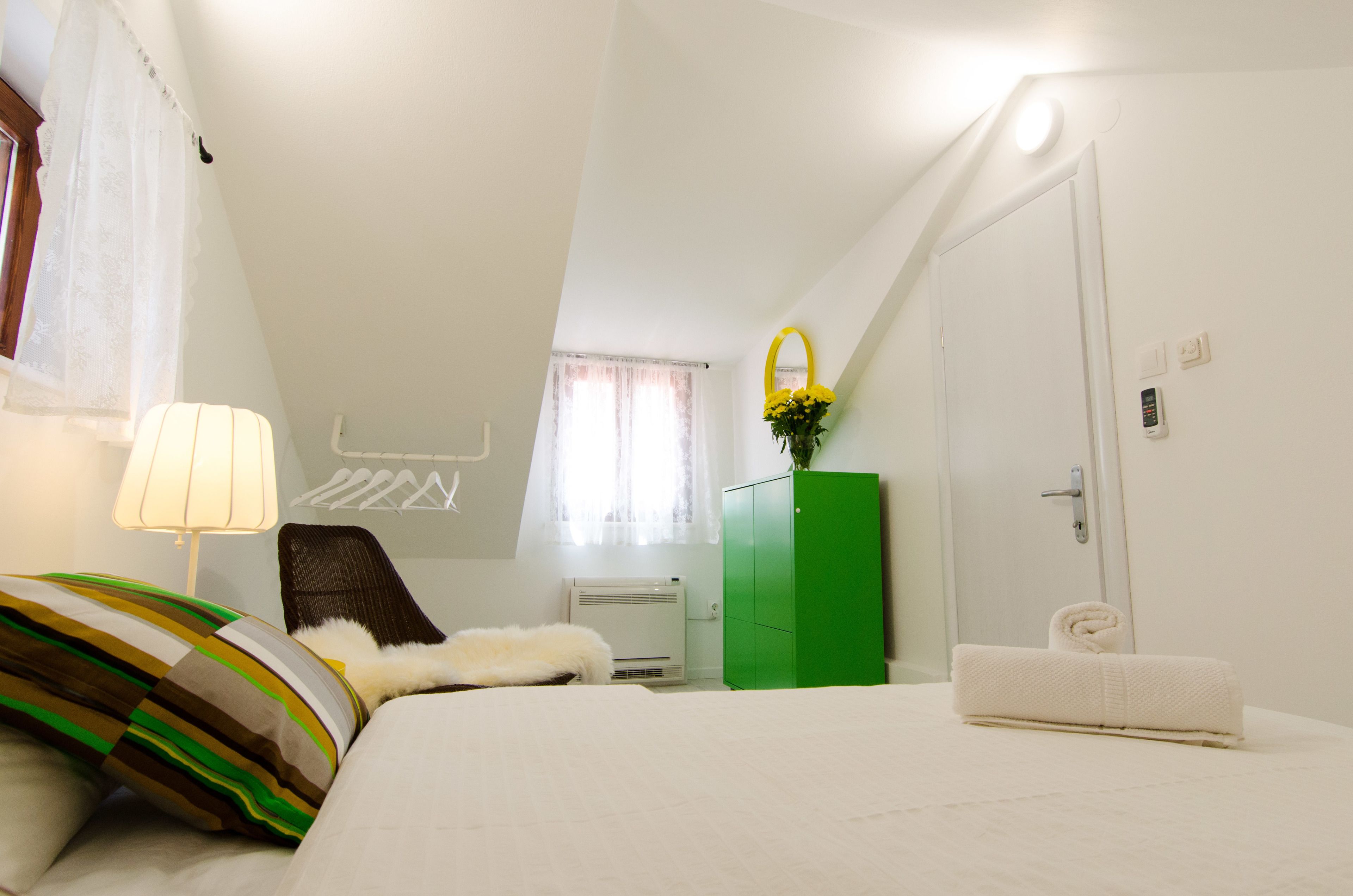 A bedroom with a bed, a green wardrobe, a white door, and a window with curtains.