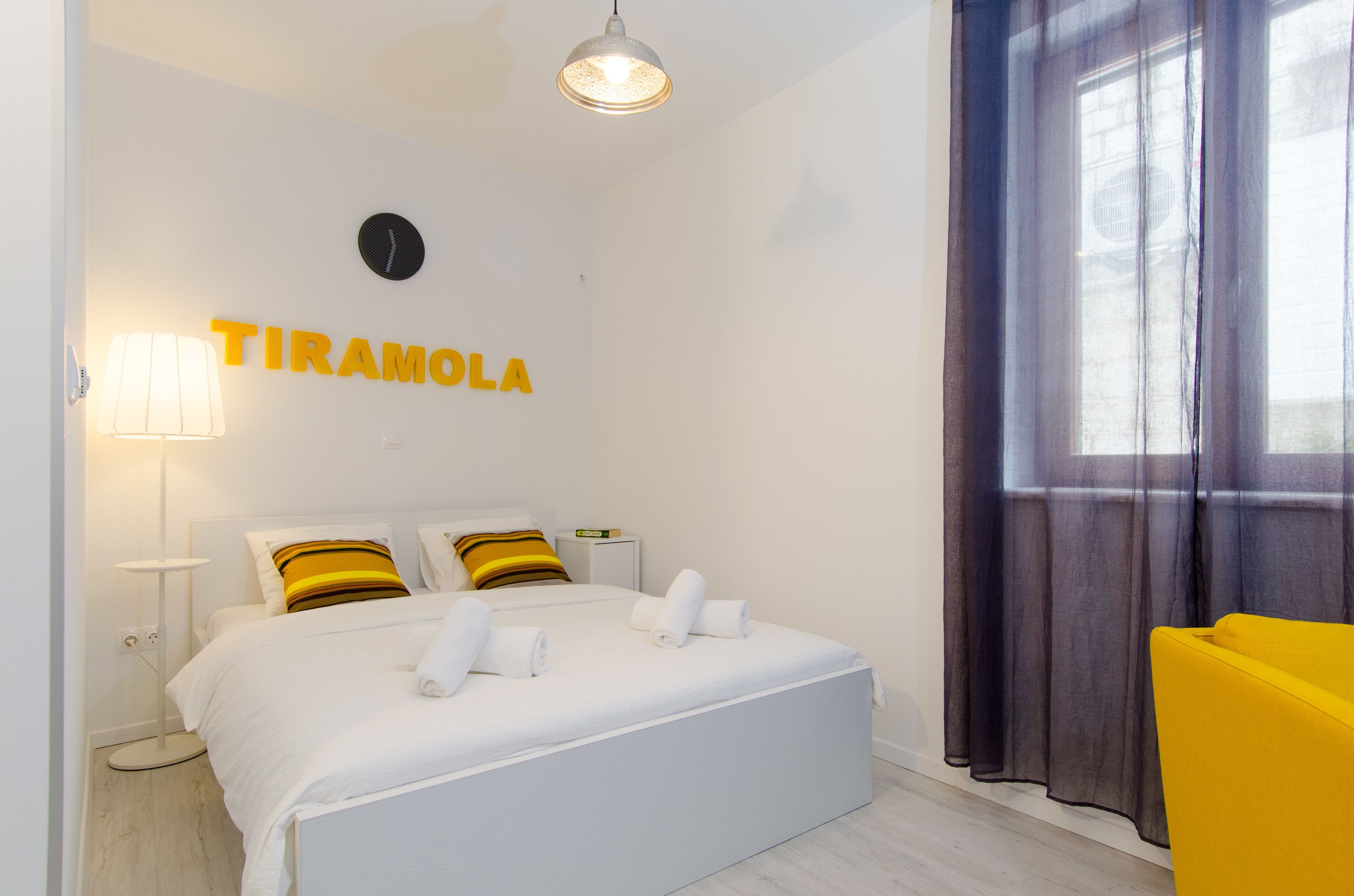 A hotel room with a bed, a nightstand, a lamp, a chair, and a window with curtains.
