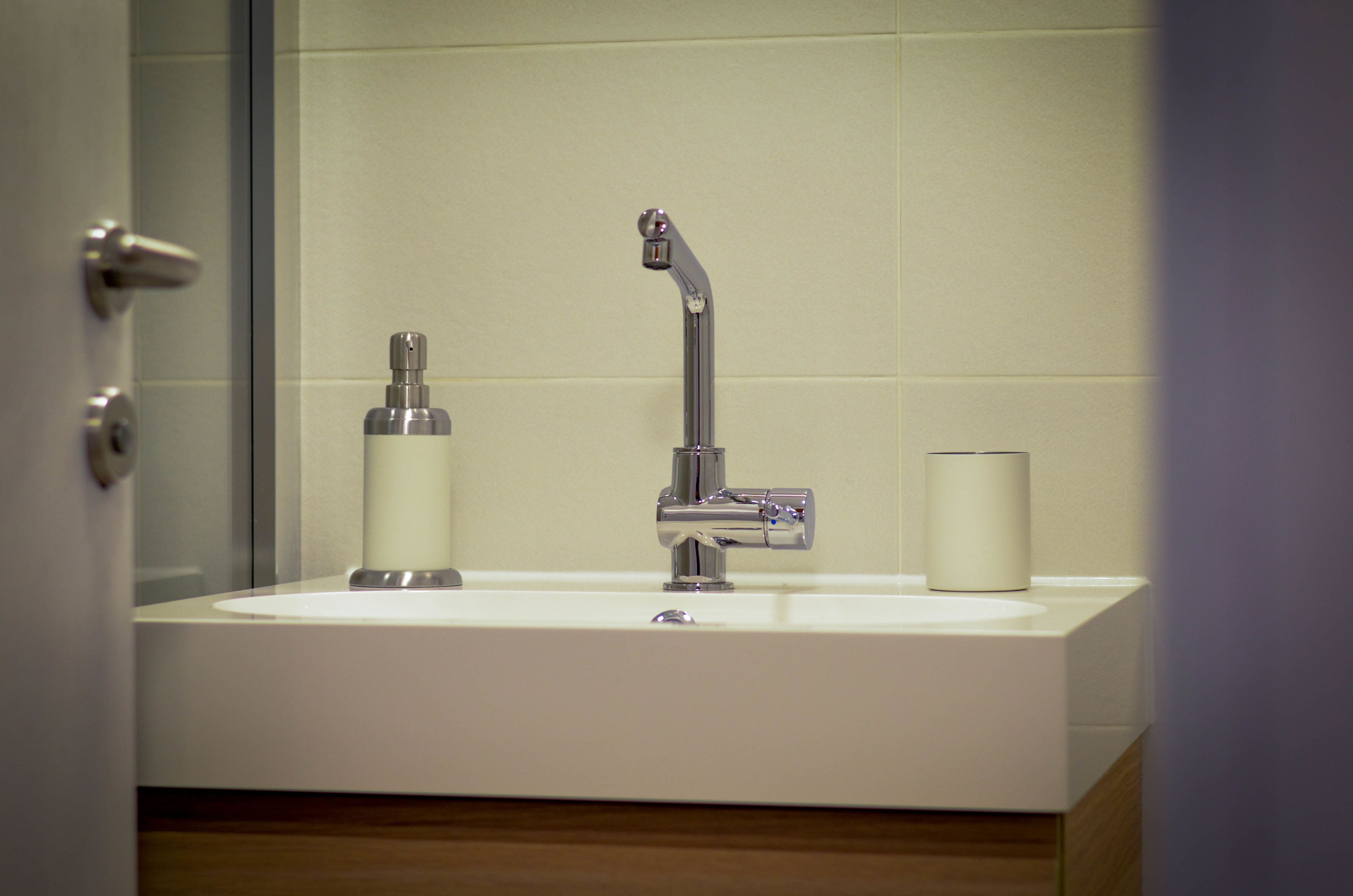Un baño con lavamanos blanco, grifo cromado y dispensador de jabón.