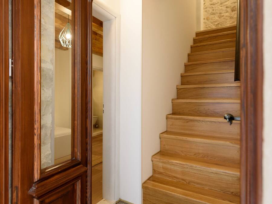Una escalera de madera con piso estampado que lleva a una habitación con pared de piedra y techo de madera.